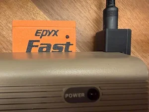 An orange Epyx Fastload cartridge and a right-angle power adapter inserted into a Commodore 42