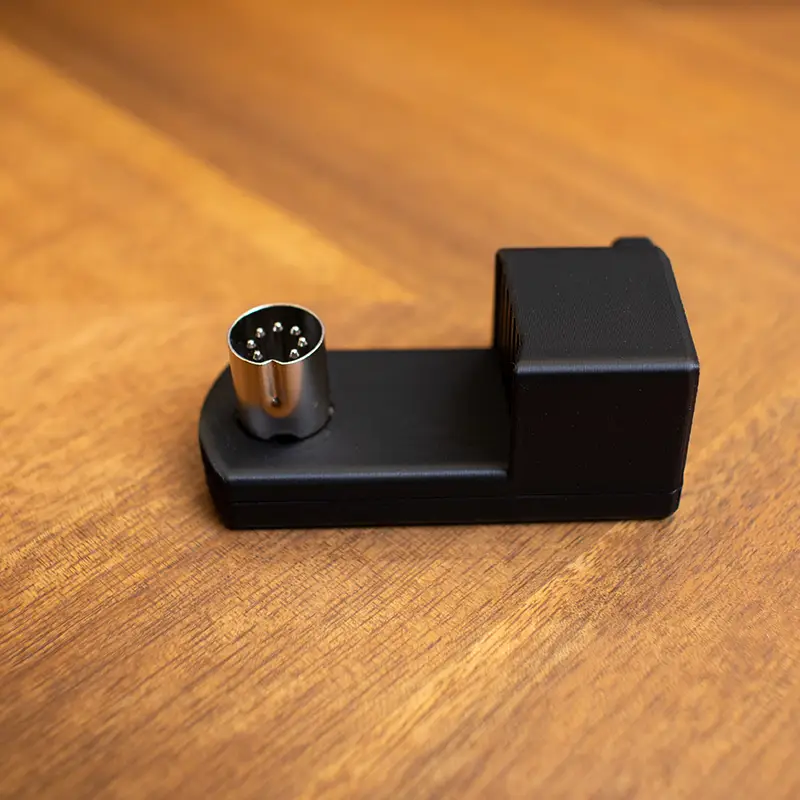 A photo of a Commodore 64 right-angle power adapter atop a wooden surface.