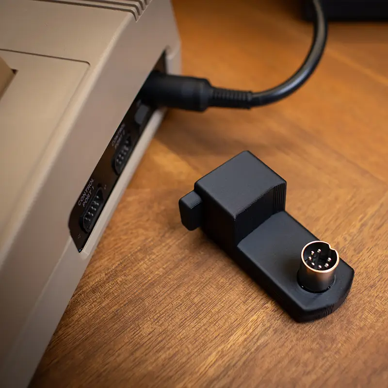 A photo of a Commodore 64 right-angle power on a desk. A C64 is beside it using a traditional plug.