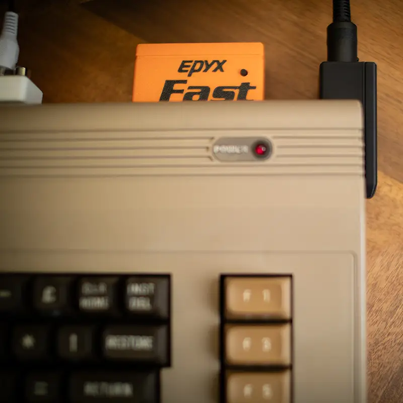 A top down view of a Commodore 64 using an Epyx FastLoad cartridge and right-angle power adapter.