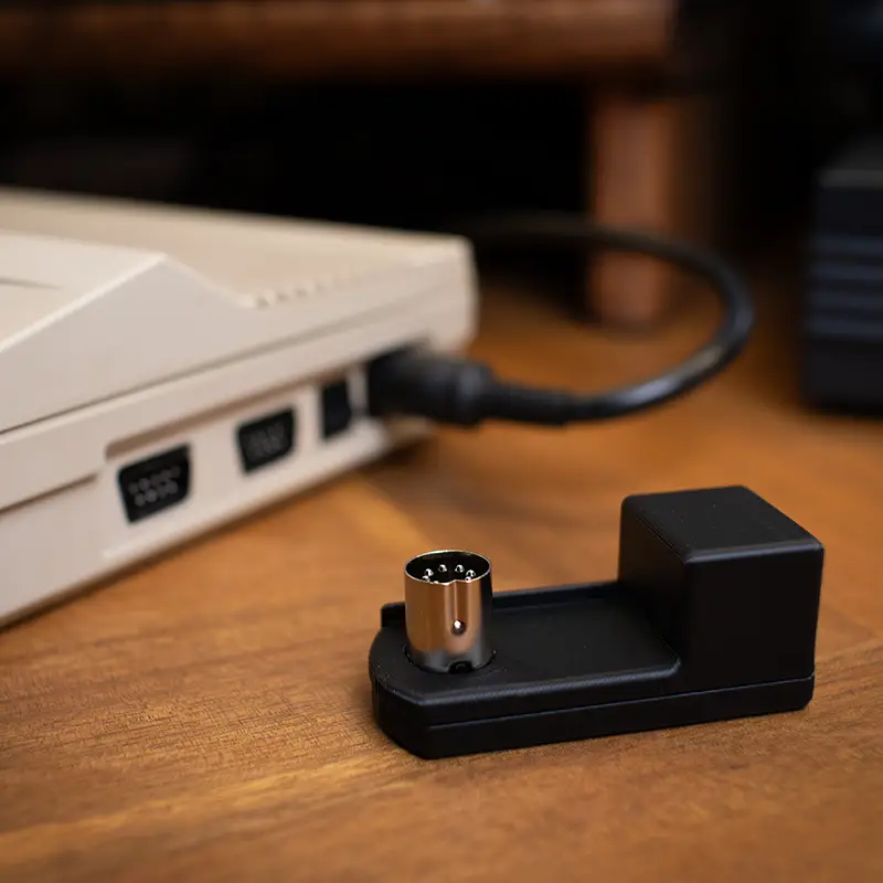 A right-angle power adapter beside a Commodore 64C. The 64C has a traditional power plug attached.