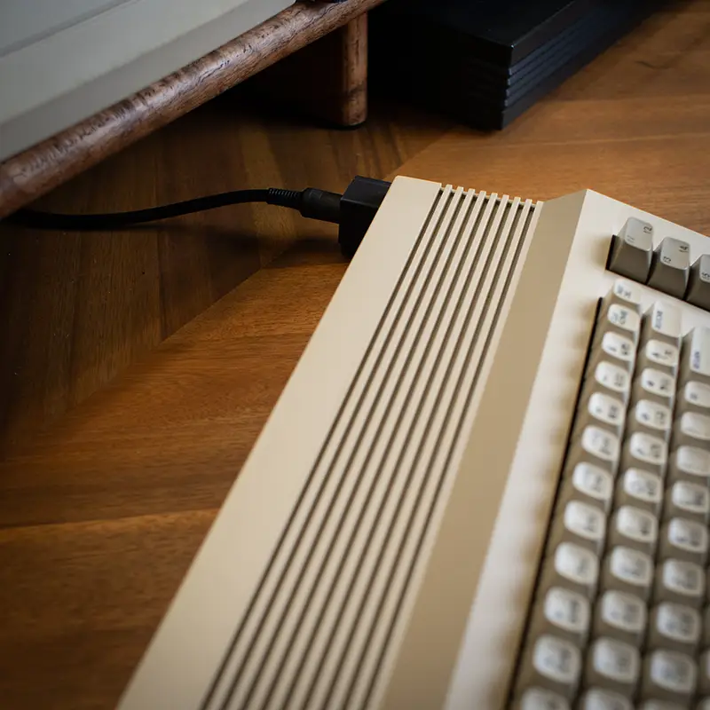 Top/back view of a Commodore 64C computer with a cable plugged into a right-angle power adapter.